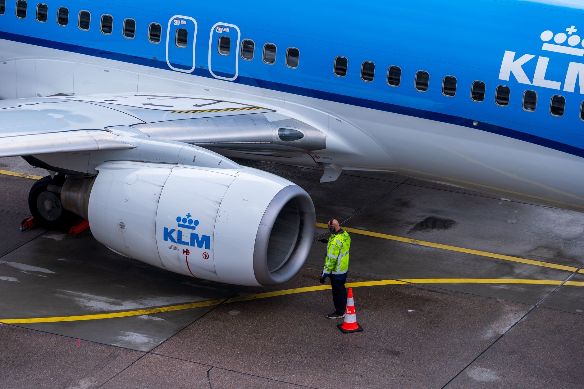 A KLM aircraft undergoing maintenance on the tarmac with an engineer inspecting it